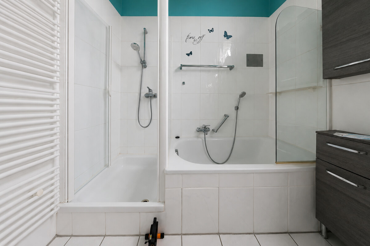 Altes Badezimmer mit Badewanne und schmaler Duschkabine in der Verlaengerung